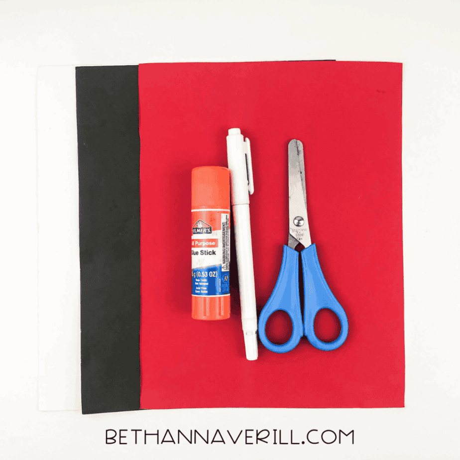 Materials laid out: red, black, and white construction paper, glue stick, scissors, and markers.