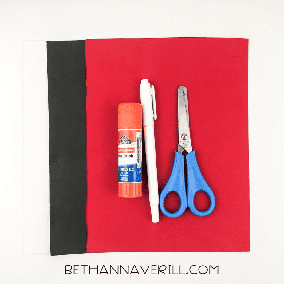 Materials laid out: red, black, and white construction paper, glue stick, scissors, and markers.