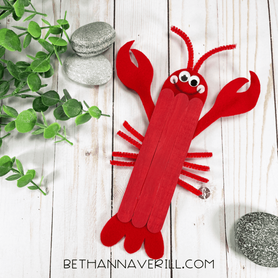 Completed popsicle stick lobster craft with googly eyes, felt claws, and pipe cleaner legs