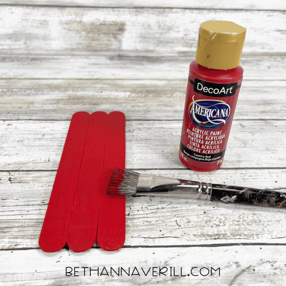 Red painted popsicle sticks with paintbrush and paint bottle
