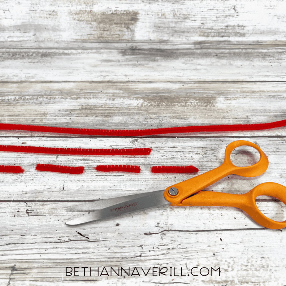 Red pipe cleaners cut into lobster legs beside scissors