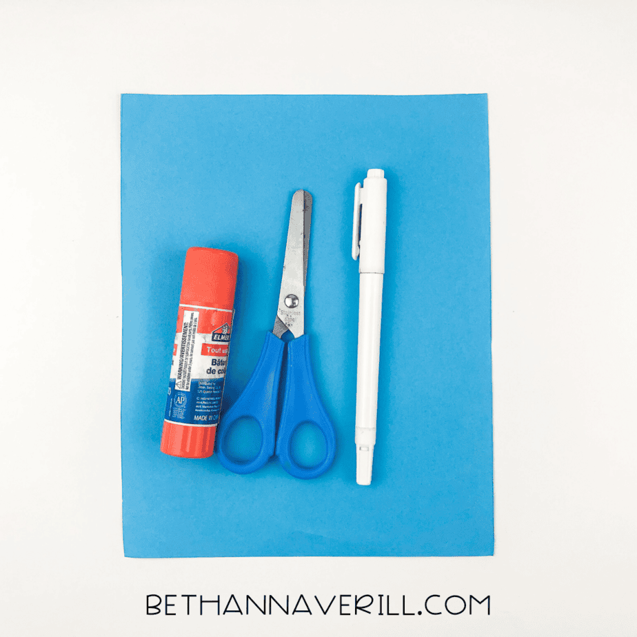 Blue construction paper, glue stick, scissors, and white pen laid out for a handprint craft.