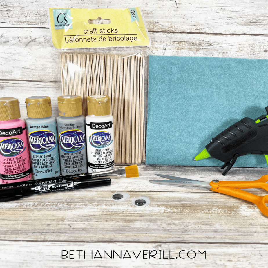 Materials laid out: craft sticks, acrylic paint, googly eyes, glue gun, scissors, and marker.