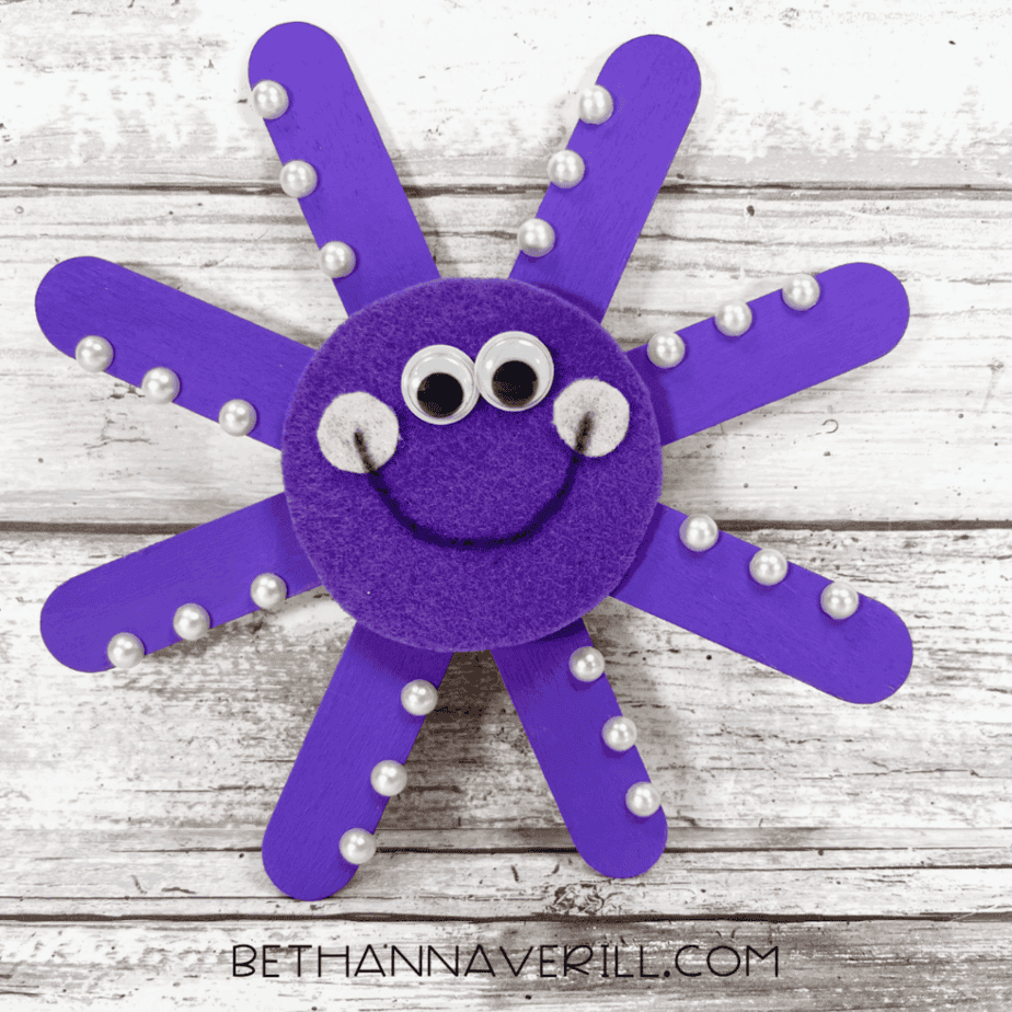 Finished purple popsicle stick octopus craft with big eyes and smile.