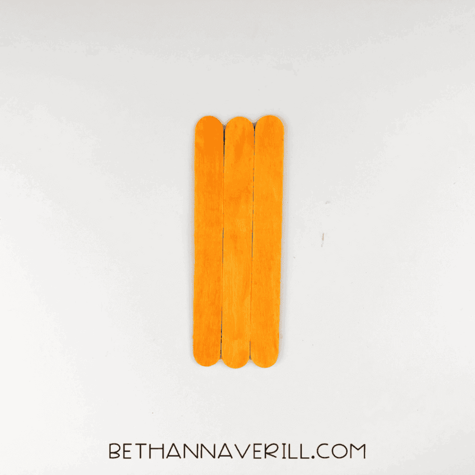 Three orange craft sticks taped together.