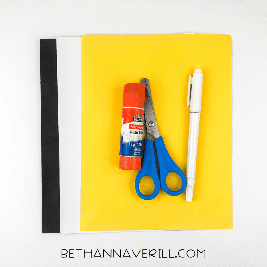 Craft supplies including black, white, and yellow paper, glue stick, scissors, and a marker