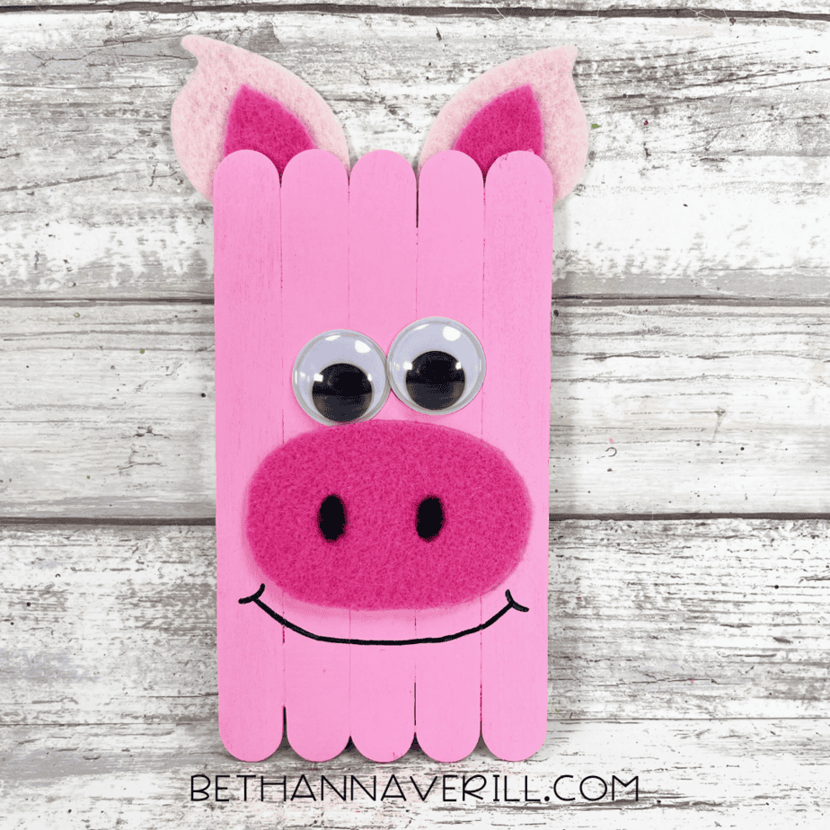 Completed pig popsicle stick craft with felt ears, snout, googly eyes, and a drawn-on smile.