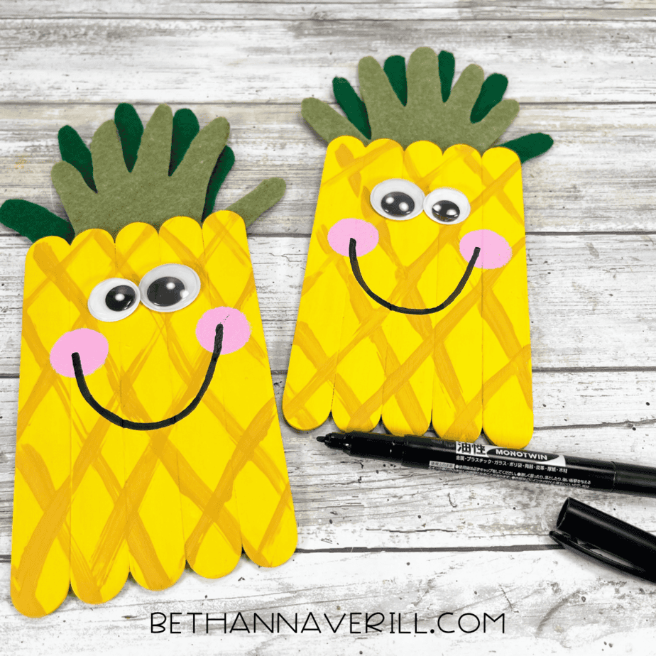 Drawing a smile — black marker adding a curved smile to the pineapple face below the googly eyes and cheeks.