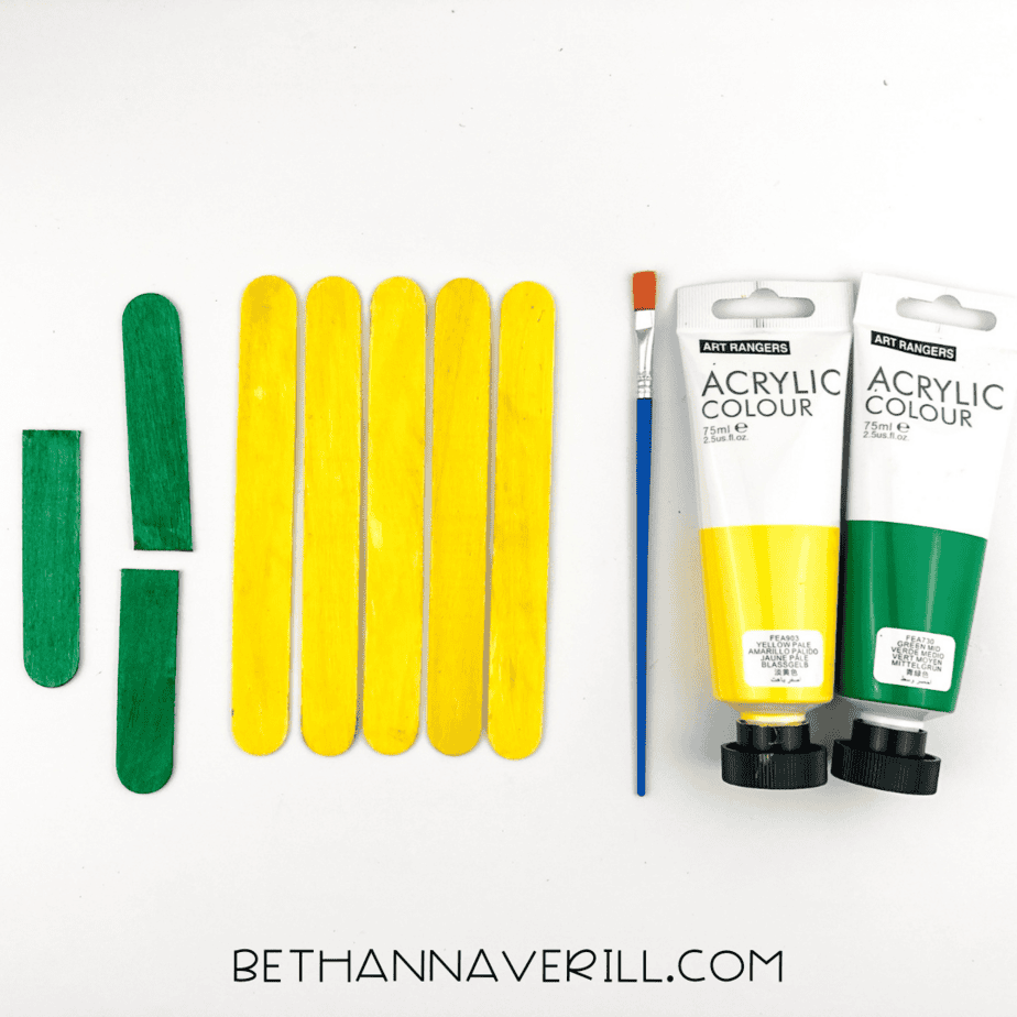 Painted popsicle sticks shown: six yellow for the body, three green halves for the leaves.