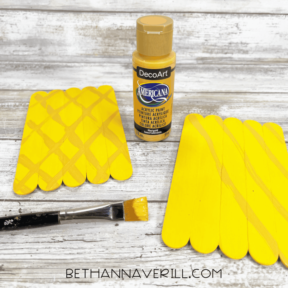 Adding crisscross lines for pineapple texture — light brown acrylic paint brushed diagonally across the yellow base to create a pineapple skin pattern.