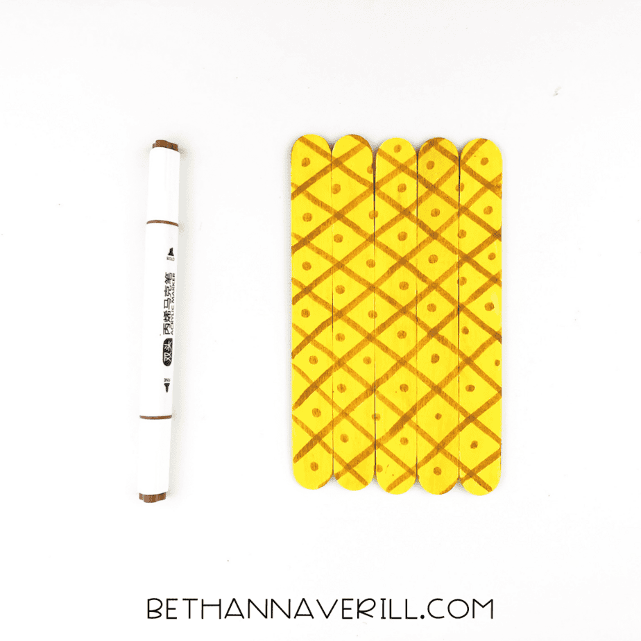 Yellow sticks decorated with crisscross lines and dots drawn using a brown marker.