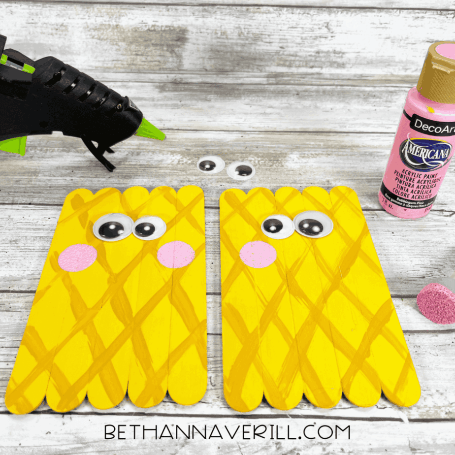 Adding eyes and cheeks — googly eyes and pink painted circles attached to the pineapple face using a hot glue gun.