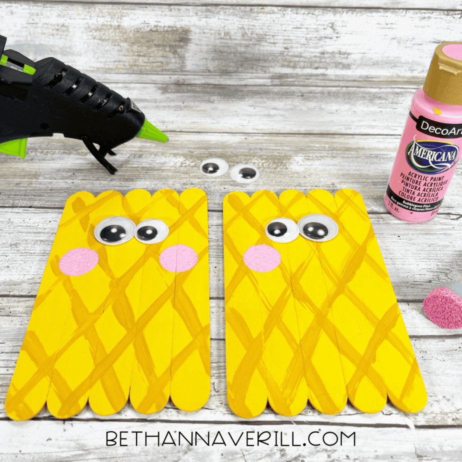 Adding eyes and cheeks — googly eyes and pink painted circles attached to the pineapple face using a hot glue gun.