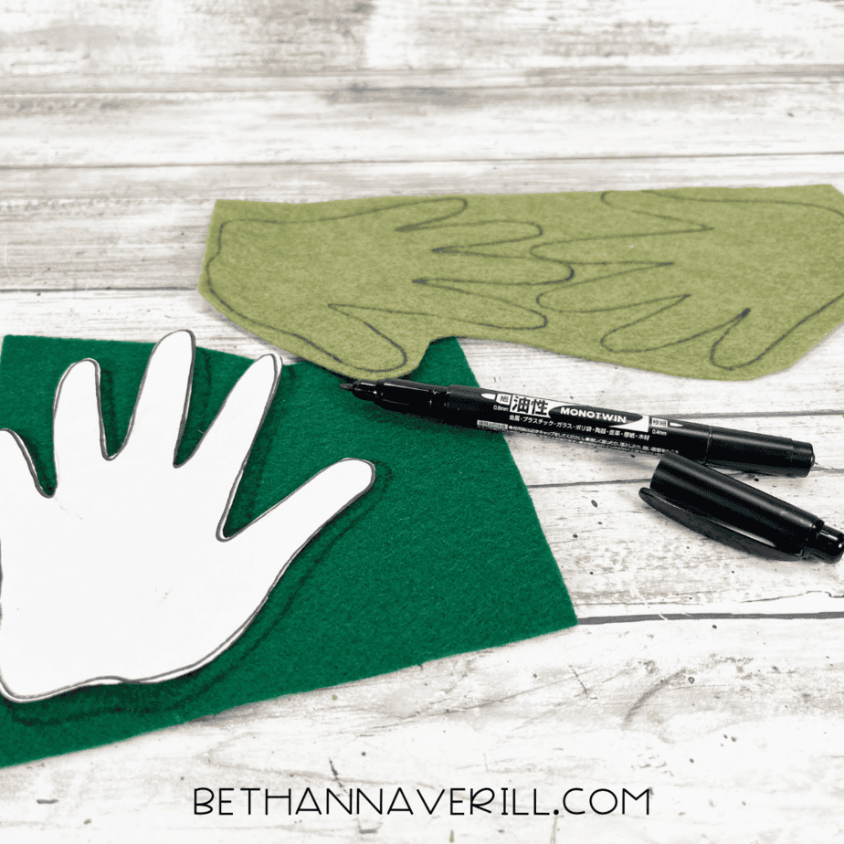 Tracing hand shapes for pineapple leaves — paper hand template traced with black marker onto green felt sheets.