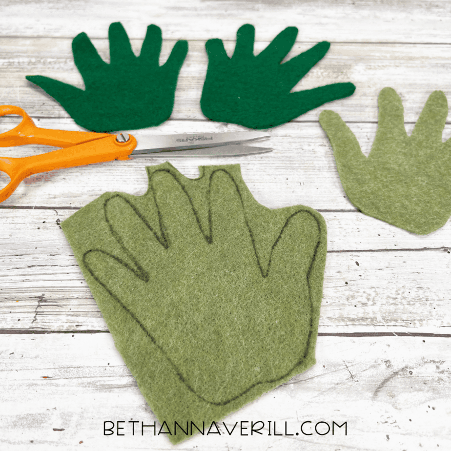 Cutting out green felt hand shapes — scissors cutting out multiple hand-shaped leaf pieces in dark and light green felt.