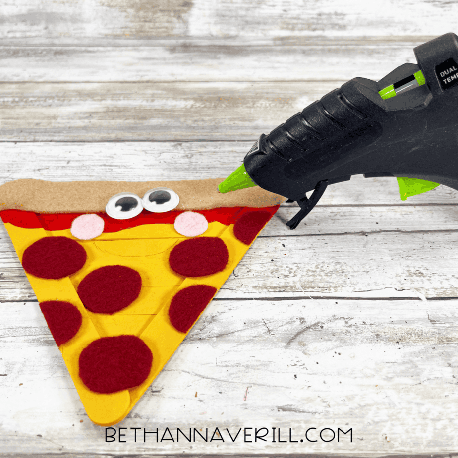 Gluing pepperoni toppings — hot glue gun attaching red felt pepperoni circles to the yellow pizza slice base.