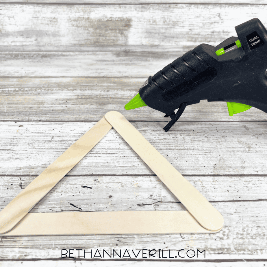 Forming a triangle with craft sticks — three wooden craft sticks being glued together at the corners with a hot glue gun.