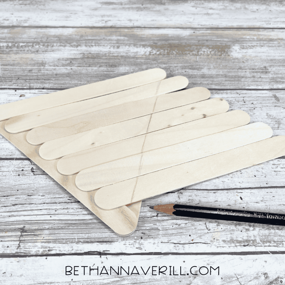 Laying craft sticks across the triangle — craft sticks placed side-by-side across the triangle frame, marked with a pencil for trimming.
