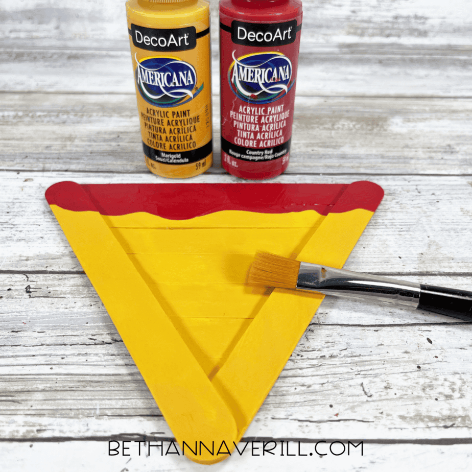 Painting the pizza slice — yellow acrylic paint for the cheese and red paint for the sauce along the top edge.