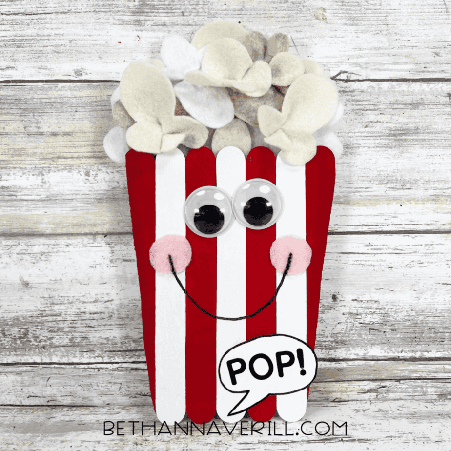 Finished popcorn craft with a big smile, rosy cheeks, googly eyes, fluffy felt popcorn, and a “POP!” speech bubble.