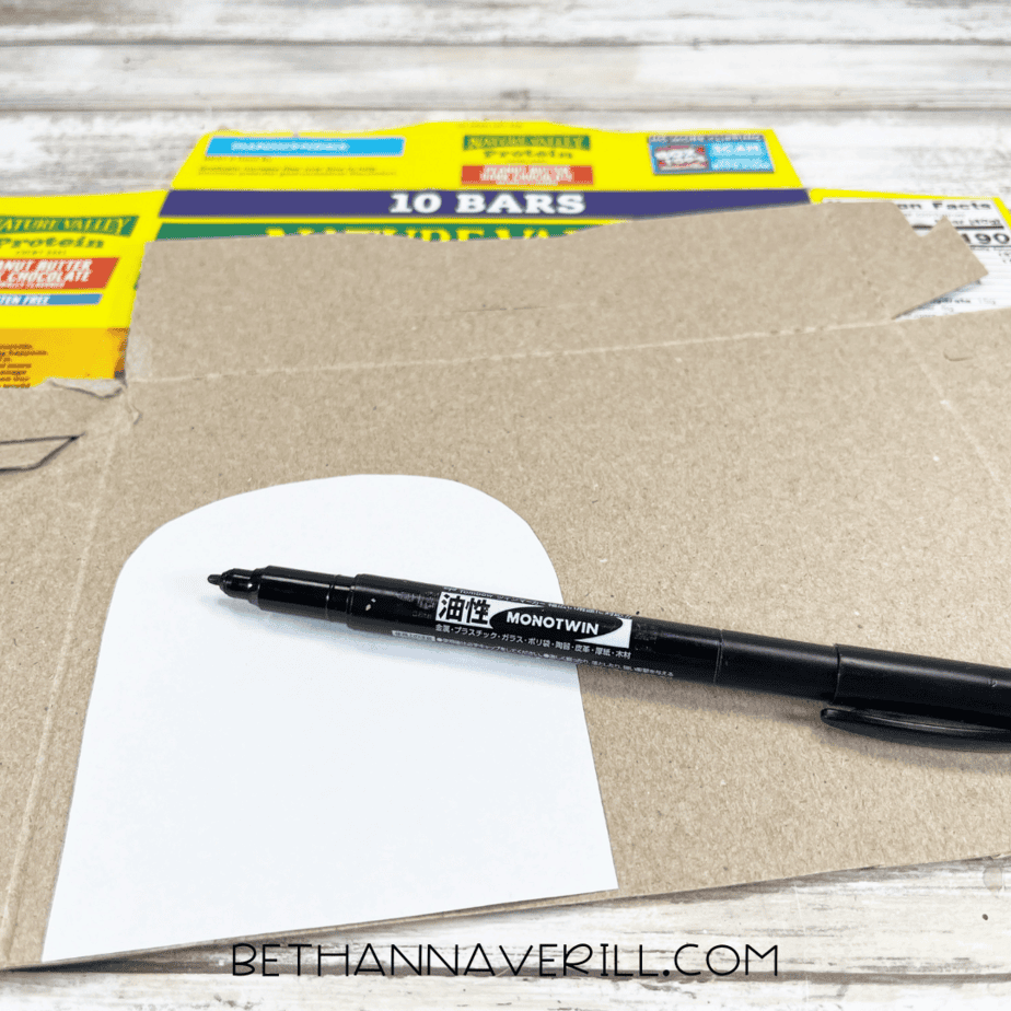 A rounded popcorn box top traced onto cardboard using a white paper template and a black marker.