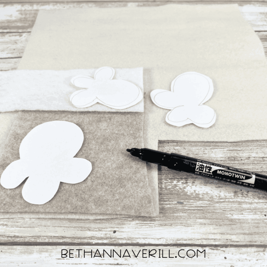 Popcorn-shaped paper templates placed on top of white, cream, and tan felt sheets with a black marker nearby.