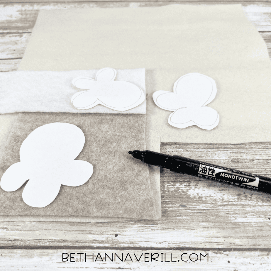 Popcorn-shaped paper templates placed on top of white, cream, and tan felt sheets with a black marker nearby.