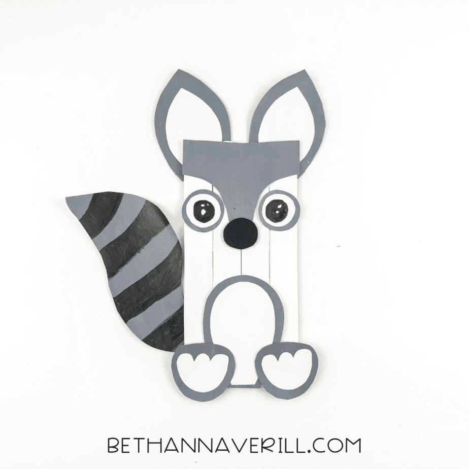 raccoon popsicle stick craft with paper mask, eyes, belly, paws, and striped tail.