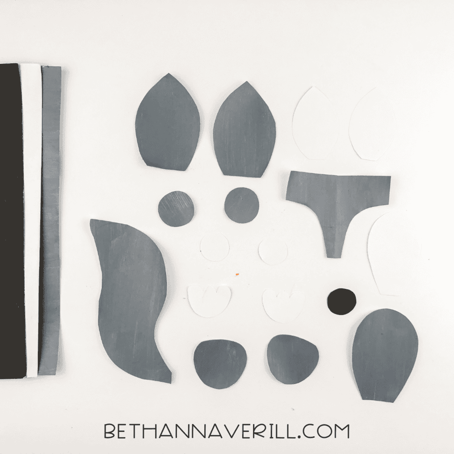 Gray and white paper shapes cut for ears, mask, belly, paws, eye pieces, tail, and a black circle nose.