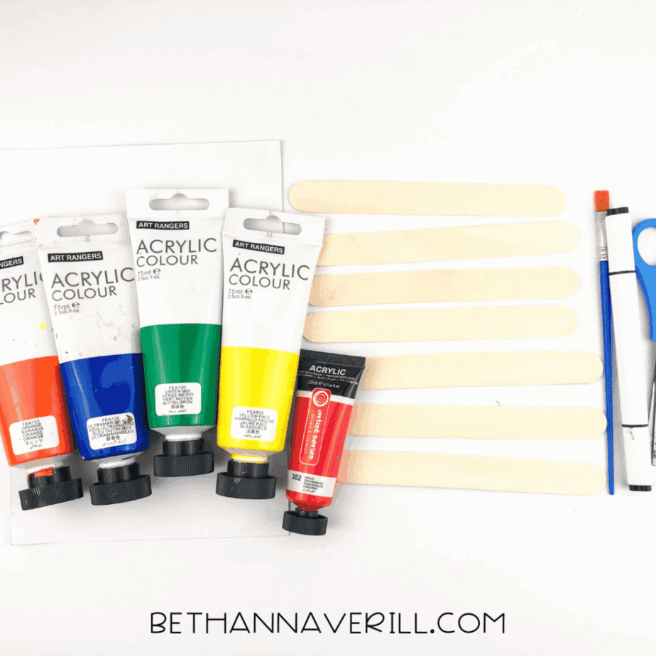Craft supplies: rainbow paints, jumbo popsicle sticks, scissors, brush, and white paper.