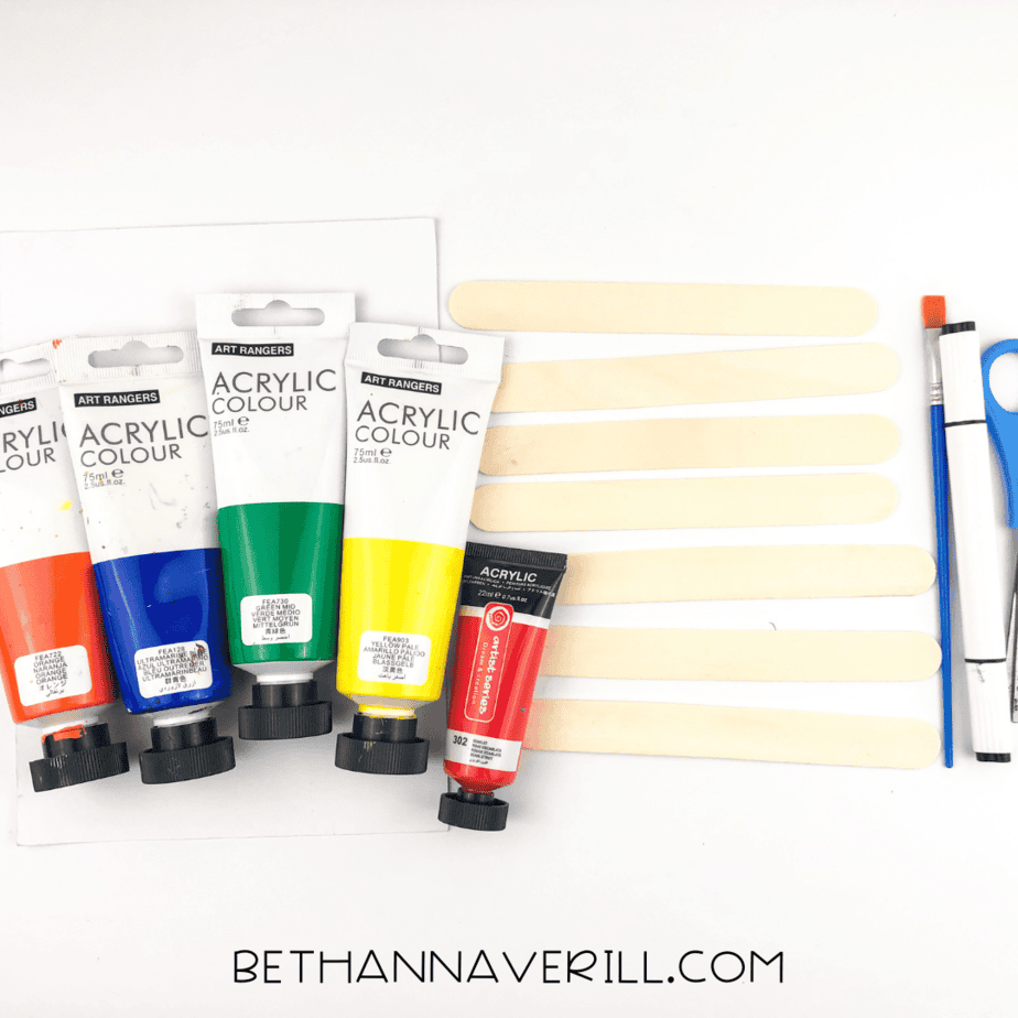 Craft supplies: rainbow paints, jumbo popsicle sticks, scissors, brush, and white paper.