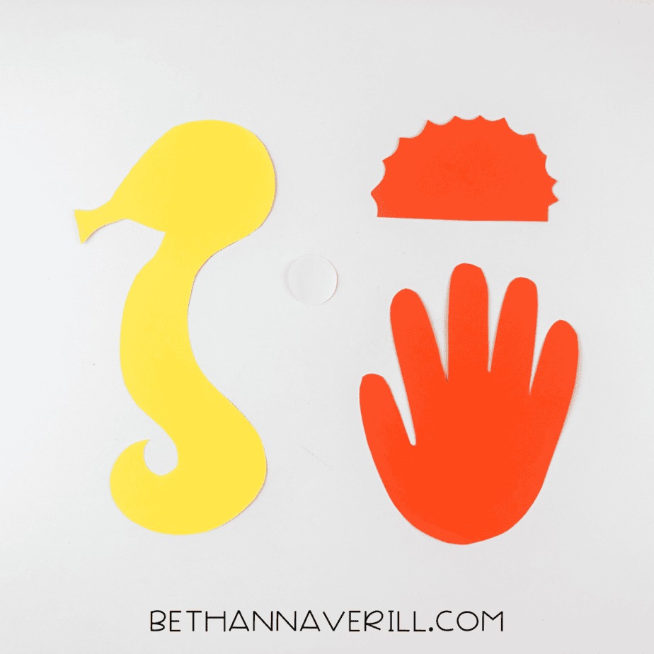Paper pieces cut out for the seahorse: yellow body, red handprint, crest, and eye.