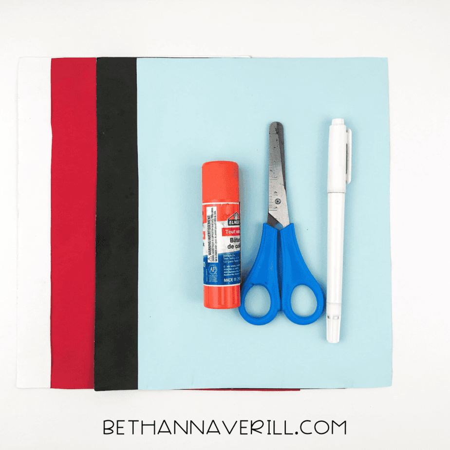 Shark handprint craft supplies: red, black, white, and blue paper, glue stick, scissors, pencil.