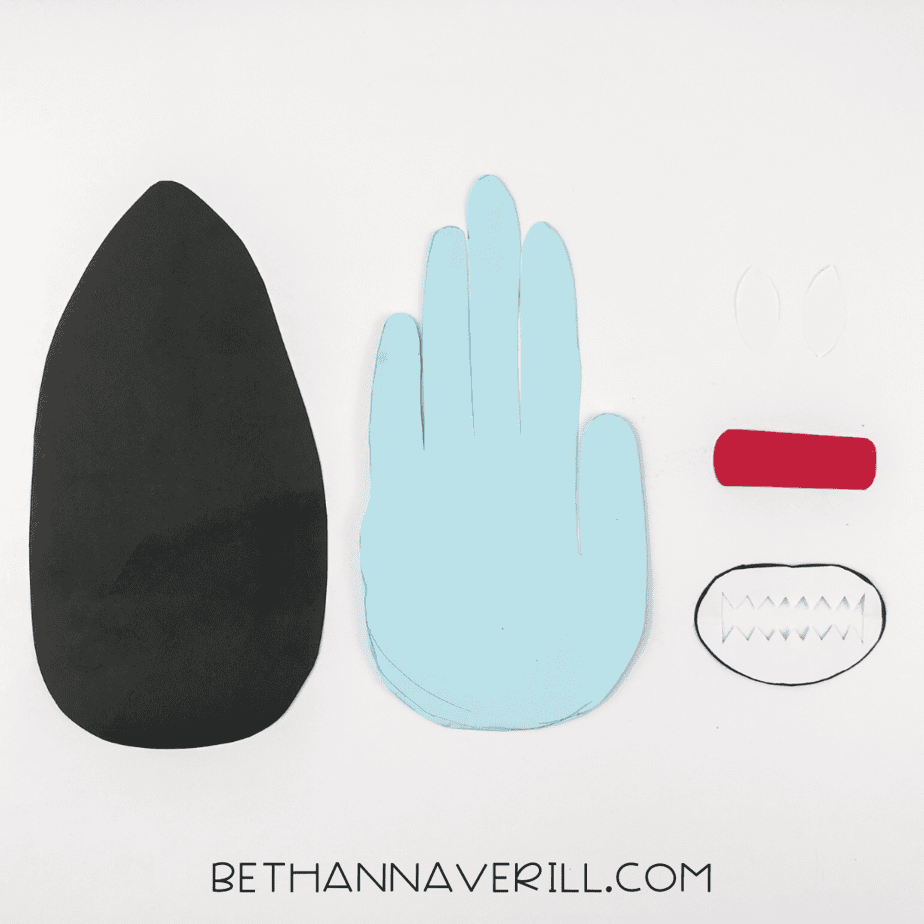 All cutout pieces for the shark handprint craft laid out, including handprint, body, mouth, and eyes.
