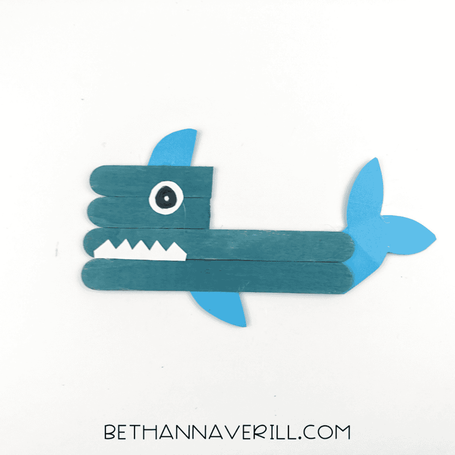 shark popsicle stick craft with drawn black pupil.