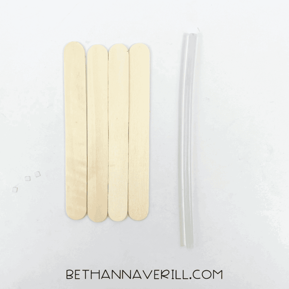Five craft sticks lined up with tape and a glue stick