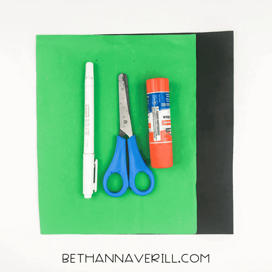 Materials for spider handprint craft: black and green paper, glue stick, scissors, pencil, and black marker