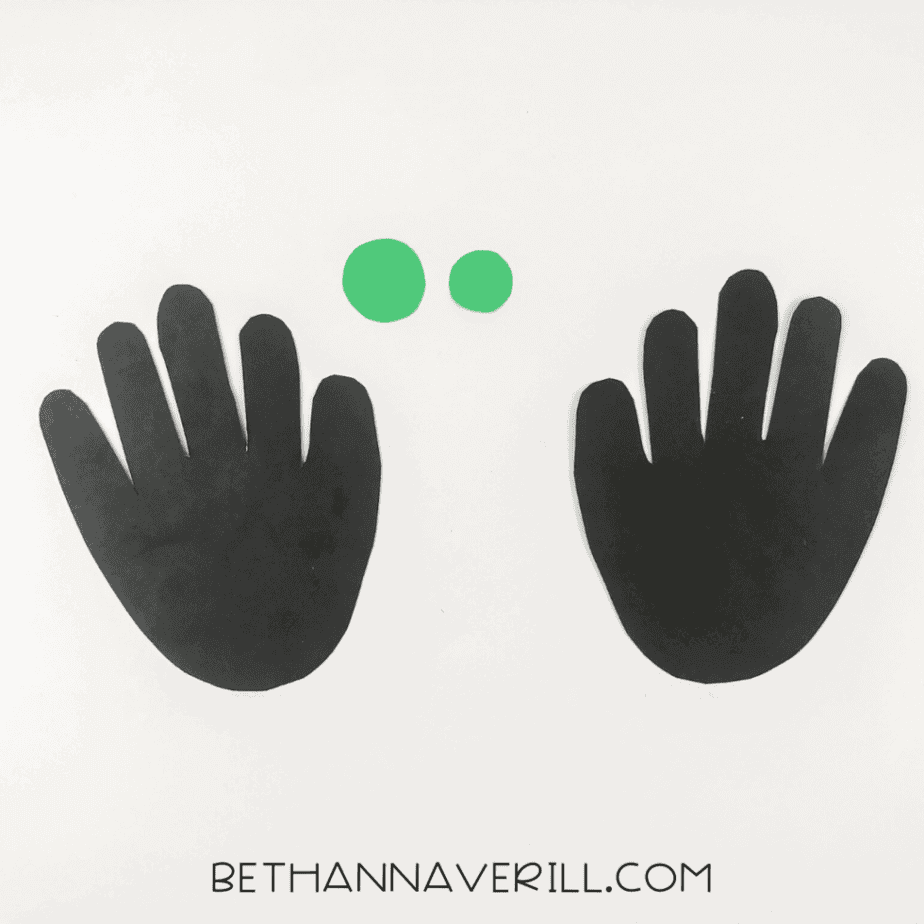 Two black handprint cutouts and two green paper circles for the eyes