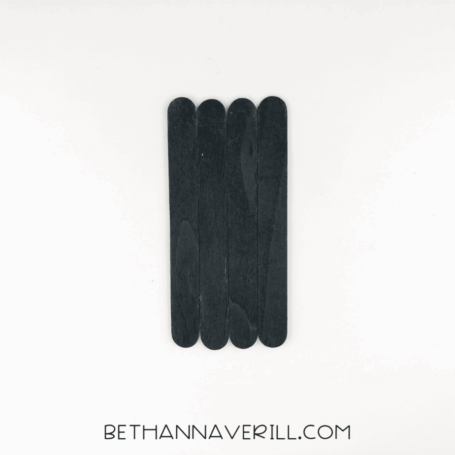 Four black sticks glued side‑by‑side to form a rectangular spider body.