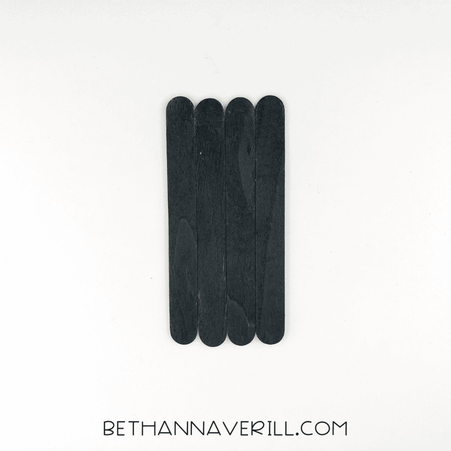 Four black sticks glued side‑by‑side to form a rectangular spider body.