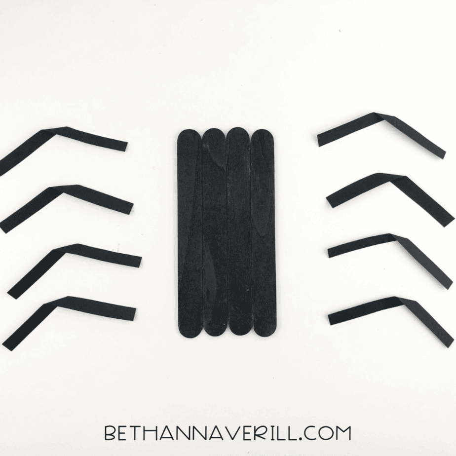 Eight paper leg strips folded to make joints, arranged around the black stick body.