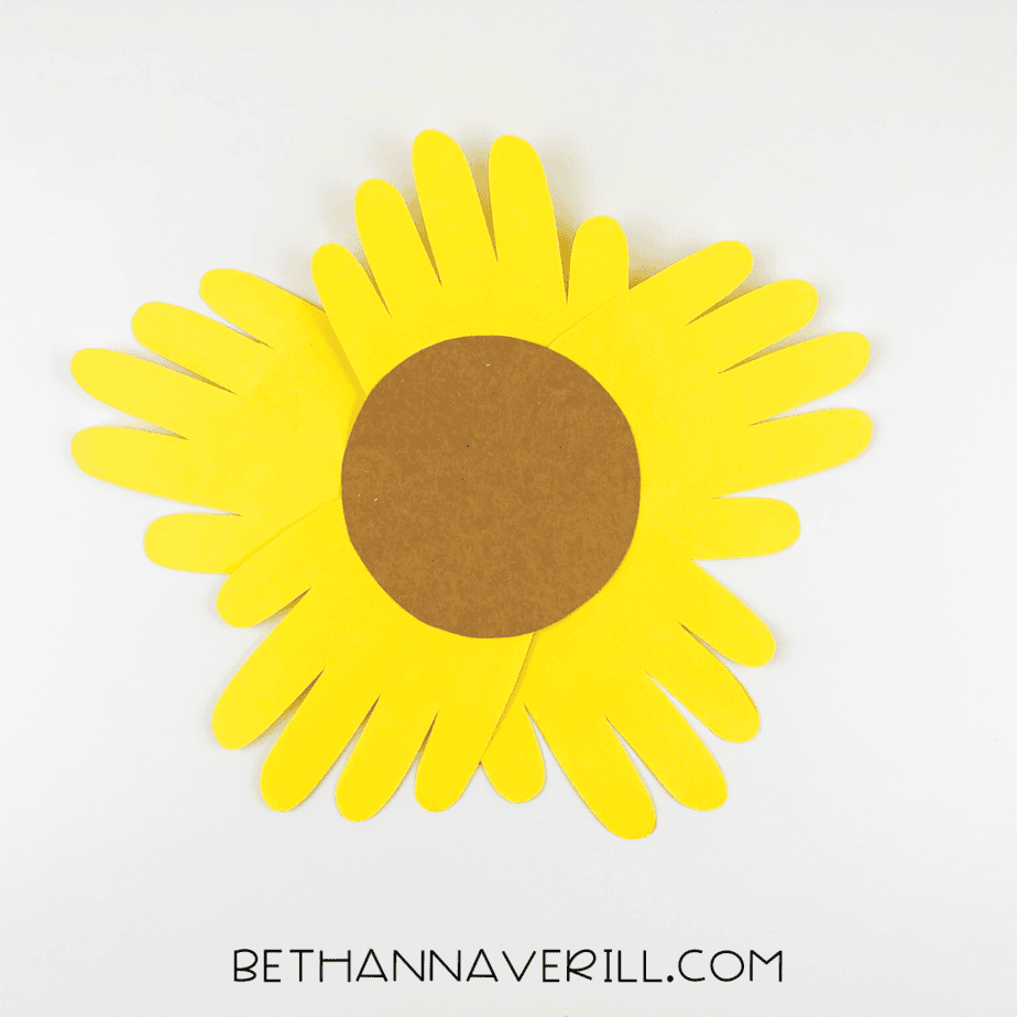 Brown circle glued in the center of yellow handprints to form sunflower face