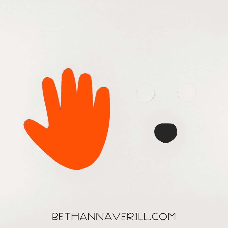 Orange handprint cutout with two white paper circles and a small black paper nose