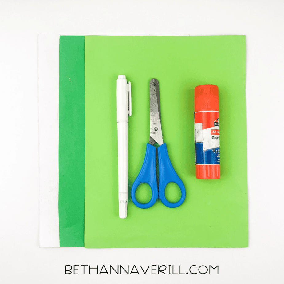 Supplies for turtle craft: green and white paper, glue stick, scissors, and black marker.