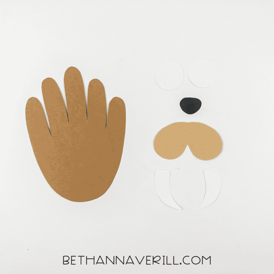 Cutout pieces: brown handprint, two white circles, black nose, two white tusks, and brown cheek ovals.