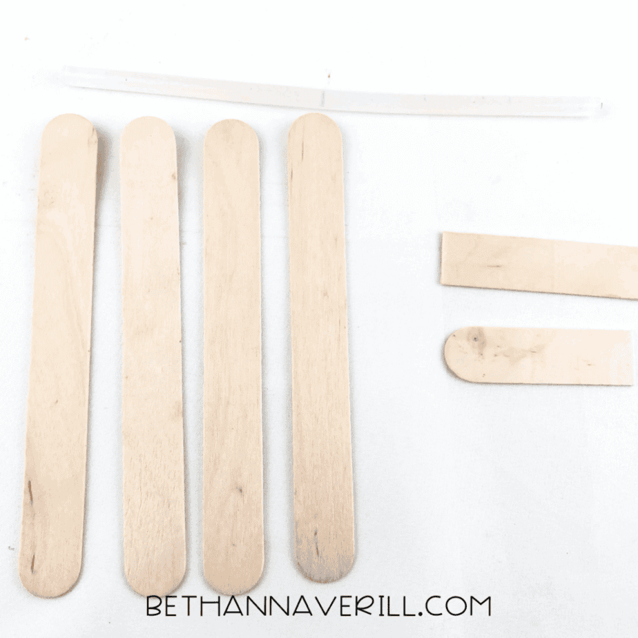 Four craft sticks lined up with two small sticks and a glue stick above.