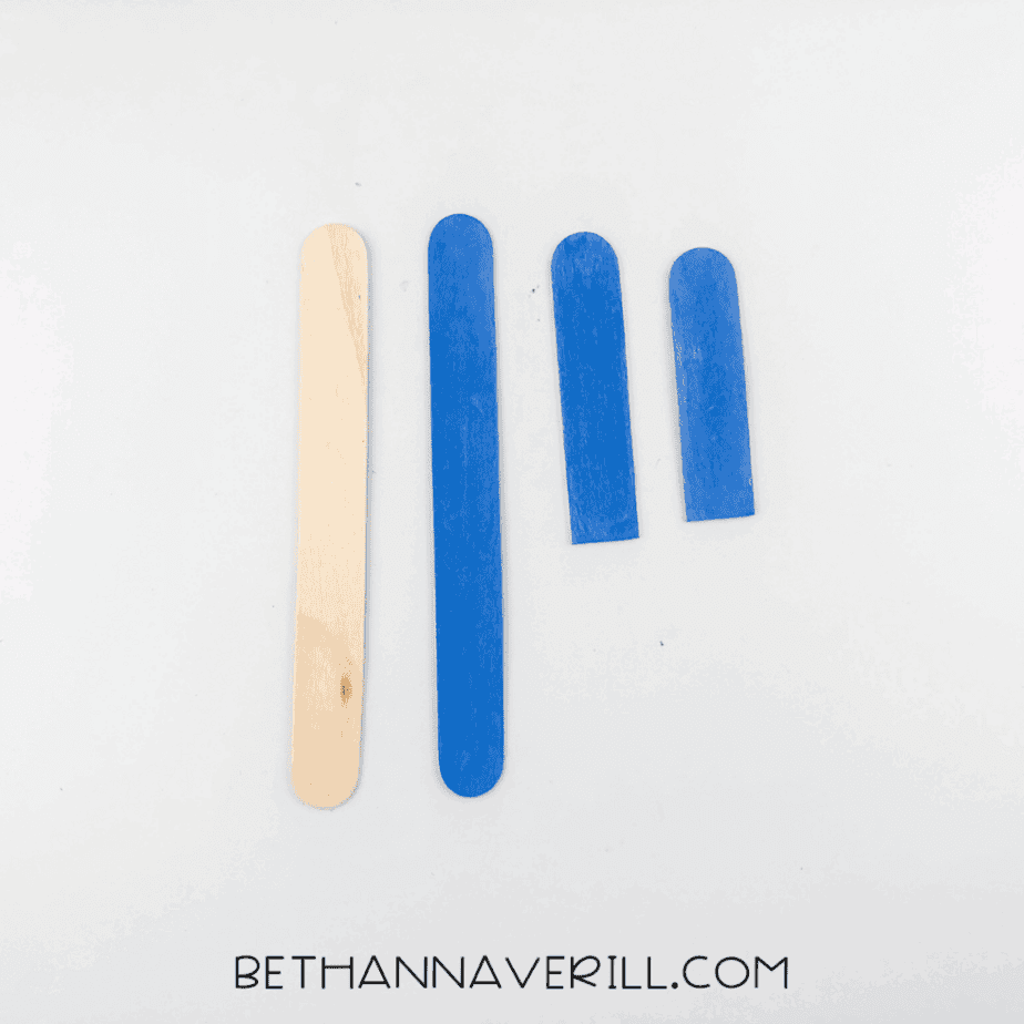 One unpainted stick next to two blue painted sticks, one of which is cut in half.