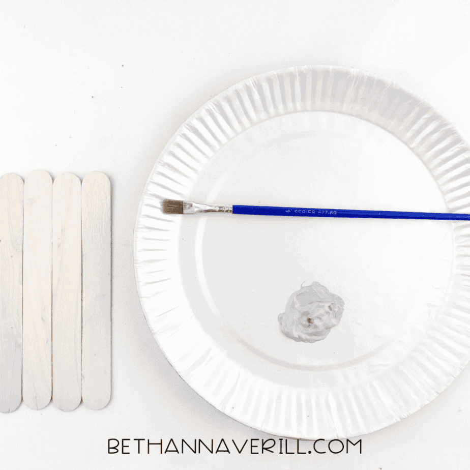 Gray paint mixed on a paper plate next to the craft sticks
