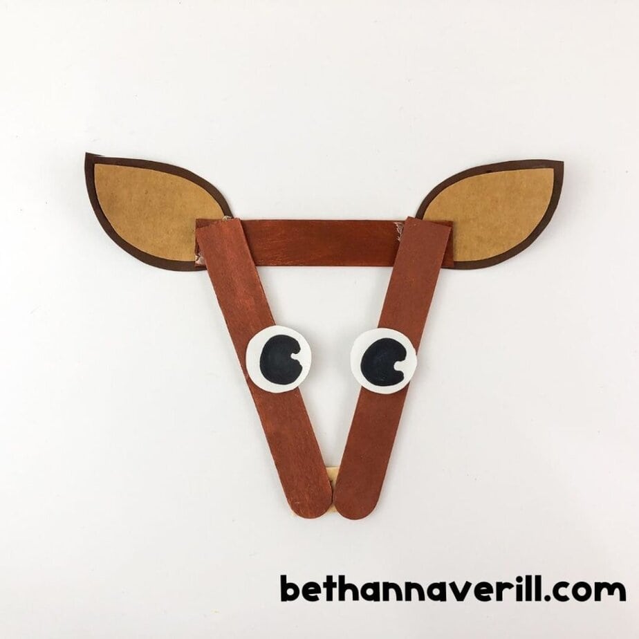 A reindeer face made from craft sticks, ears, and googly eyes, without antlers or nose attached yet.