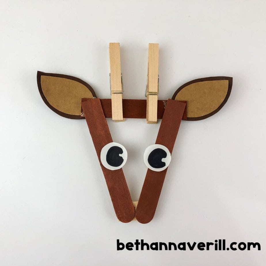 Partially completed reindeer face with paper ears, googly eyes, and two clothespins clipped at the top to act as antlers.